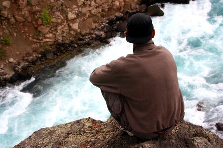 a young man perched on a rock overlooking the river belowの写真素材