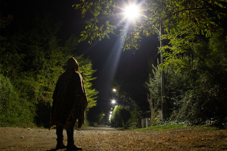 A man with a hood walks along the road in the night.の写真素材