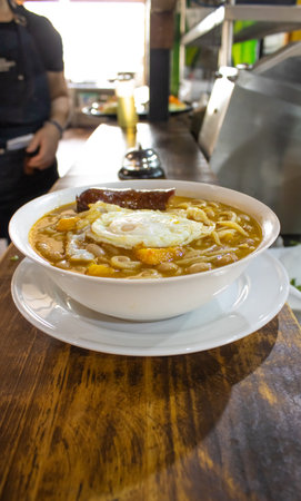 Thai noodle soup with fried egg in white bowl on wooden tableの写真素材