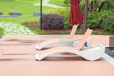 Wicker deck chair and table in the beautiful summer park with green lawns and flowerbed
