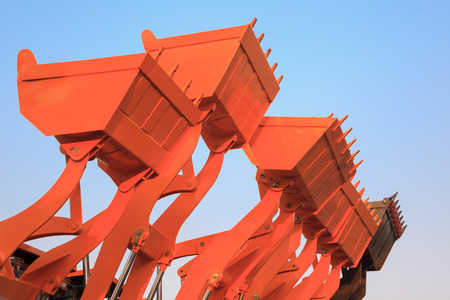 Part of modern yellow excavator machines,the buckets/shovels raised against blue sky in a construction site.の写真素材