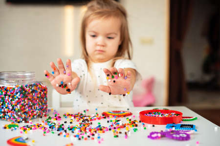 Little blonde girl makes a toy with thermo mosaic. Plastic thermomosaic handmade, modern hobby for children. Modeling, sensory education, design with hot plastic, fine motor skills developmentの写真素材