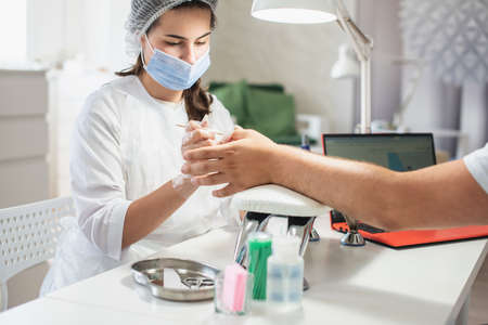 Girl manicurist doing manicure for man. Man professional manicure at the beauty spa salon. Male body care. Relaxing, caring about nails, spa treatment. Manicure specialist and clientの写真素材