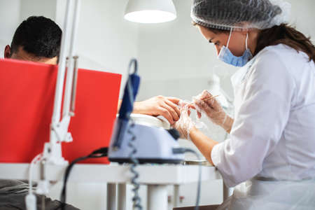 Girl manicurist doing manicure for man. Man professional manicure at the beauty spa salon. Male body care. Relaxing, caring about nails, spa treatment. Manicure specialist and clientの写真素材