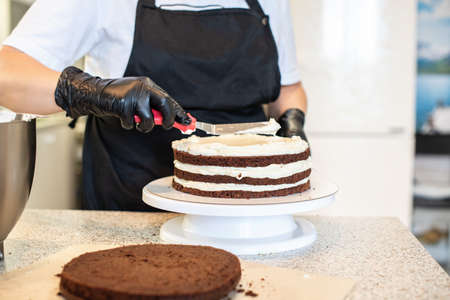 Pastry chef cook confectioner or baker in black gloves and black kitchen apron makes a cake. Home...