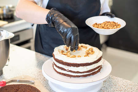 Pastry chef cook confectioner or baker in black gloves and black kitchen apron makes a cake. Home...