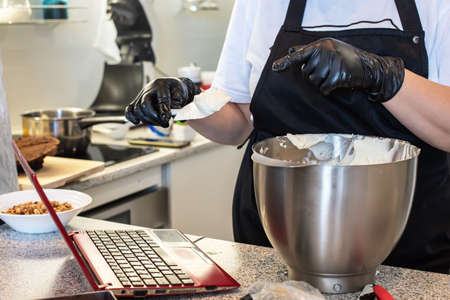 Pastry chef cook confectioner or baker in black gloves and black kitchen apron makes a cake. Home...