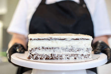 Pastry chef cook confectioner or baker in black gloves and black kitchen apron makes a cake. Home...