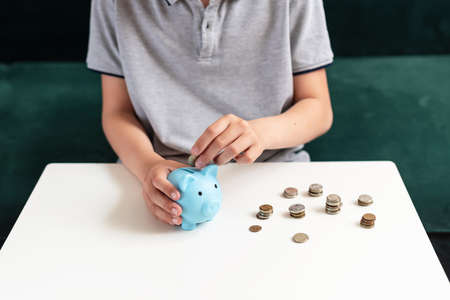 Kid teen boy saving money putting coins in a piggy bank. Learning financial responsibility and projecting savings. The concept of saving money, finance, business and investment, Lessons in mindfulnessの写真素材