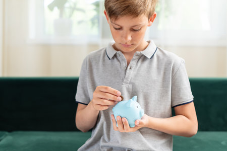 Kid teen boy saving money putting coins in a piggy bank. Learning financial responsibility and projecting savings. The concept of saving money, finance, business and investment, Lessons in mindfulnessの写真素材