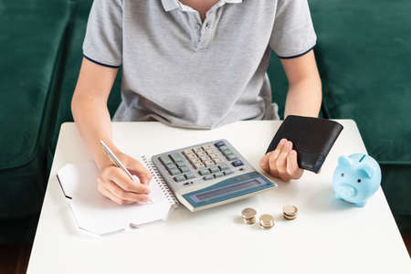 Kid teen boy counting money and taking notes, saving money in a piggy bank. Learning financial responsibility and projecting savings. Concept of finance, business, investment. Lessons in mindfulnessの写真素材
