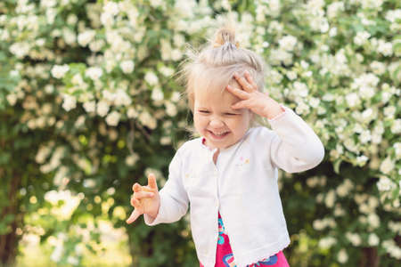 Little girl in the park on a sunny day. Todler girl in garden, under the flowering tree. Spring petals rain. Concept of spring, happy childhood, peace in the world, peace and happiness, harmonyの写真素材