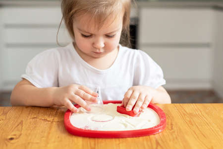 Sand art therapy, litlle girl painted on a table with sand. Sensory plays at home, playing in the semolina at kitchen, development of fine motor skills, Activities Montessoriの写真素材