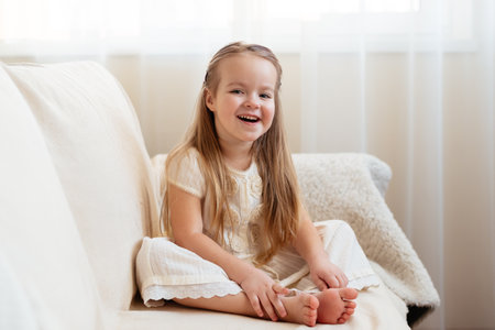 Little cute blond girl sitting on a sofa.の写真素材
