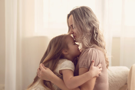 Smiling preschool girl sitting on mommies lap at home. Carefree mom and little girl laughing while playing at home. Love, warm family relationships. Happy kid with mum spending free time togetherの写真素材