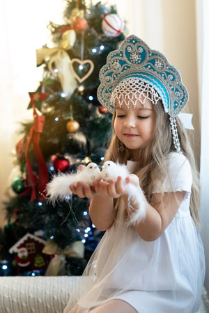 Caucasian young girl in traditional hat holding birds by Christmas tree.の写真素材