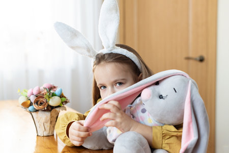 Young caucasian girl with bunny ears and stuffed rabbit at easter celebration.