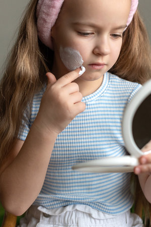 Young caucasian female child applying facial cream with mirror and headband.の写真素材