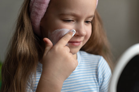 Young caucasian girl applying facial cream with mirror reflection.の写真素材
