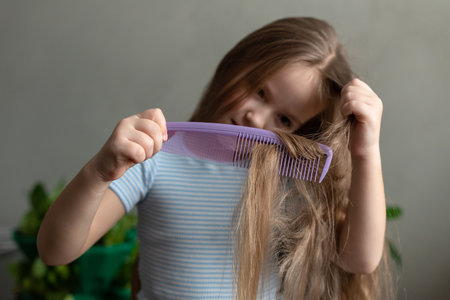 Young caucasian girl combining long hair with purple comb in striped shirt.の写真素材