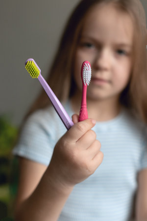 Young caucasian girl holding two toothbrushes in focused hand.の写真素材