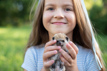Smiling caucasian young girl holding hedgehog outdoors in sunlit garden.の写真素材