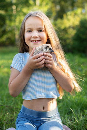 Caucasian young girl holding hedgehog in green park setting, bright sunny day.の写真素材