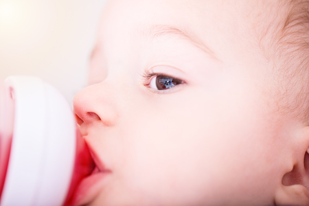 Happy baby boy drinks juice from bottle sitting on chair. Close up portrait.の写真素材
