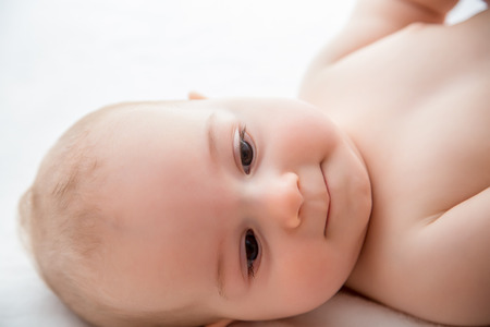 Sweet little boy with friendly attitude play in white sunny bedroom. Close-up portrait of a beautiful sleeping baby boy. Newborn, childhood theme.Textile and bedding for kids. Family morning at home. New born kid during tummy time with toy bear.の写真素材