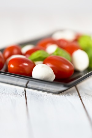 Fresh mozzarella cheese balls with cherry tomatoes and green basil isolated on white background....