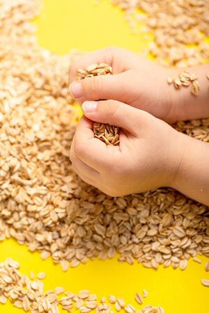 Healthy food. Raw oat flakes in children hands enclosed in the safe hands of the parent from above....