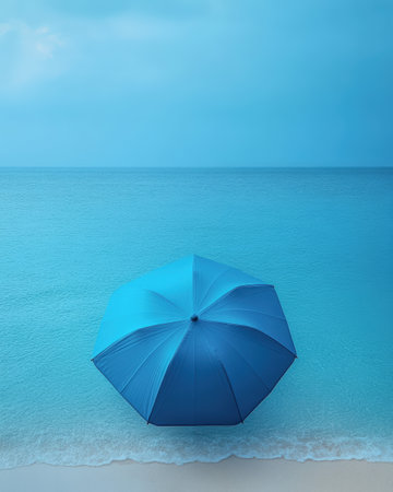 A striking blue umbrella is positioned on a sandy beach with gentle waves in the background, creating a serene and tropical vacation ambiance.の素材