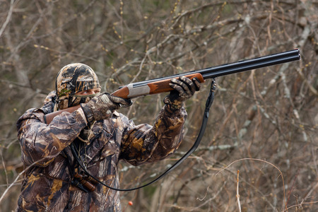 hunter in camouflage takes aim from a gun