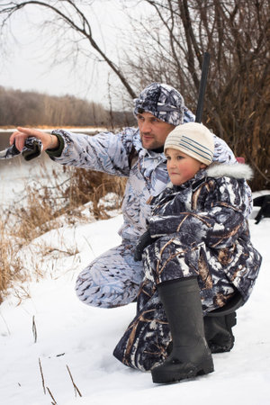 hunter shows his son where the prey on the riverの写真素材