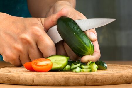 hands of woman slicing cucumber on the cutting board for salad, closeup
