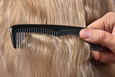 hand of hairdresser combing blonde hair, closeupの写真素材