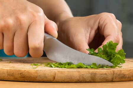 hands of woman chopping parsley leaves on the wooden cutting board