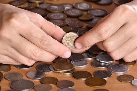 hand holding a coin among heap of coins on wooden backgroundの写真素材
