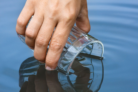 hand scooping water from a clean pond with a glass