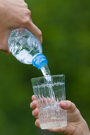 hand pouring water from bottle into glass on the green blurred backgroundの写真素材