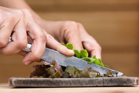 hands cutting green fresh lettuce on the wooden cutting boardの写真素材