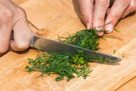 hands cutting fresh dill on the wooden cutting boardの写真素材