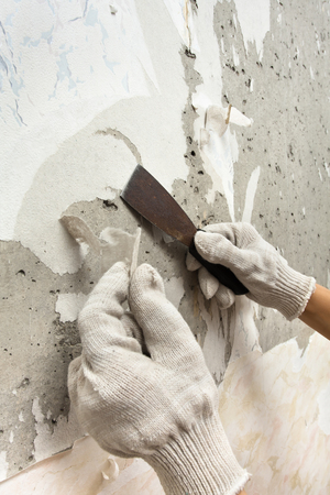 hands scraping off old wet wallpaper with spatulaの写真素材