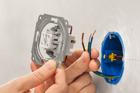 hands of electrician installing light switch in plasterboard wall during repair