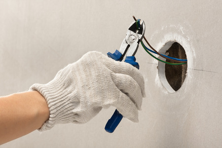 hand of electrician in gloves cutting wires with clippers during repairの写真素材