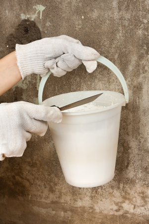 hands of plasterer holding bucket with plaster and spatula on the concrete wall backgroundの写真素材