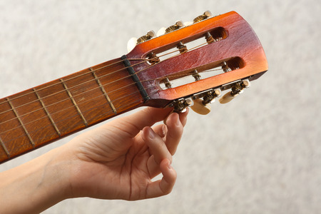hand tuning acoustic guitar from headstock, closeup