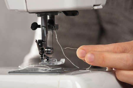 hand of seamstress insert a thread into the needle of sewing machine