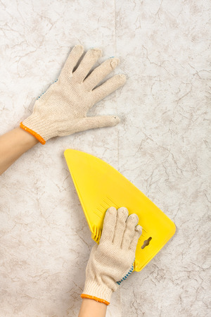 hands with spatula smoothing wallpaper on the wall during repairの写真素材