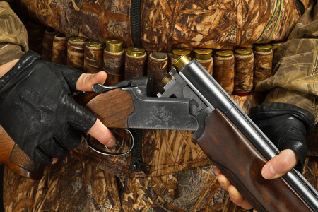 hands of hunter in camouflage holding the double-barreled shotgun, closeup